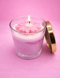 Pink floral candle in a glass container with a gold lid on a pink background
