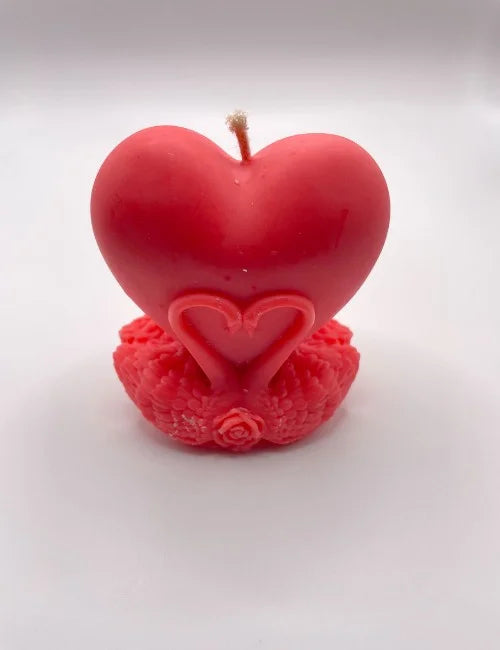 A vibrant red heart-shaped soy candle with intricate swan and rose detailing at the base.