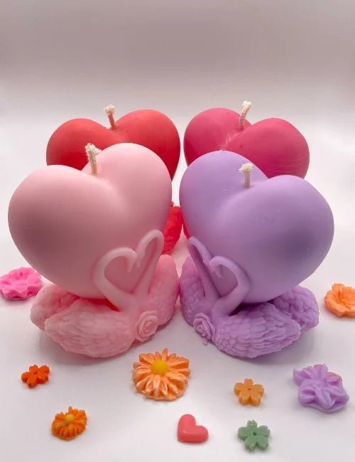 Four heart-shaped soy candles in pink, red, dark pink, and lavender colors, arranged with decorative flowers.