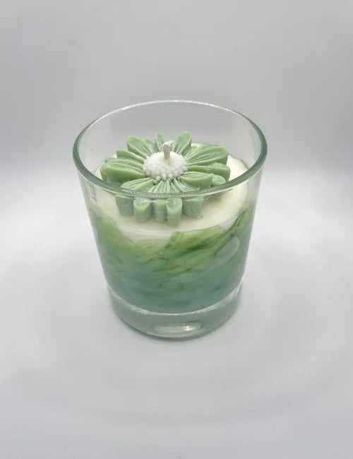 Soy candle with a green and white marbled design and a flower-shaped wax embellishment.