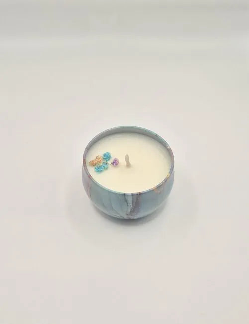 Soy candle in a purple tin with green floral decorations and a fresh meadow-inspired scent.