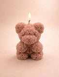 Handcrafted teddy bear soy wax candle by Aura Bliss with a lit wick on a soft neutral background