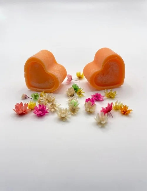 Orange natural wax melts shaped like hearts, surrounded by colorful dried flowers.