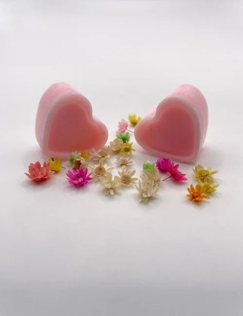 Pink natural wax melts shaped like hearts, surrounded by colorful dried flowers.