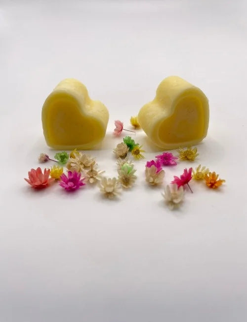 Yellow natural wax melts shaped like hearts, surrounded by colorful dried flowers.