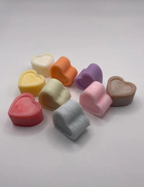 Assorted natural wax melts shaped like hearts in vibrant colors arranged with colorful dried flowers.