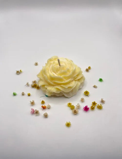 A bright yellow natural candle sculpted in the form of a rose with decorative flowers around it.