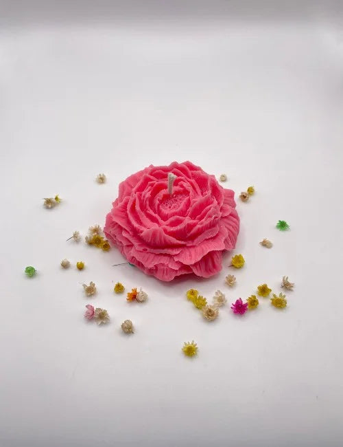 A dark pink natural candle crafted to look like a blooming rose with small decorative flowers surrounding it.