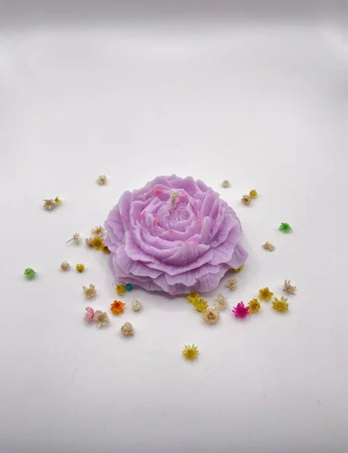 A handcrafted purple natural candle in the shape of a blooming rose with small decorative flowers around it.