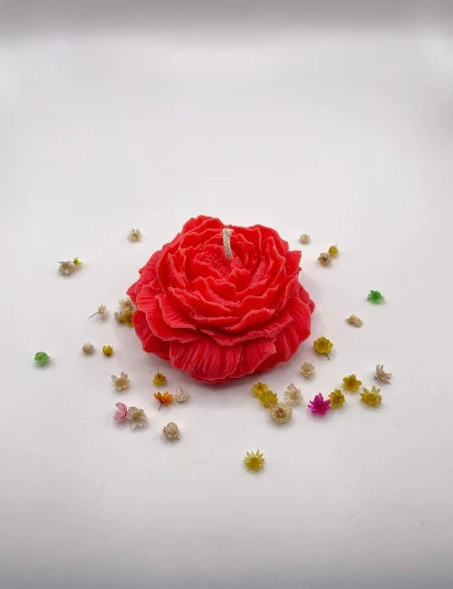 A red handcrafted natural candle resembling a rose, surrounded by small decorative flowers.