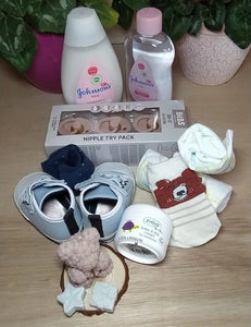 A close-up image of the baby hamper contents, including baby lotion, baby oil, pacifiers, socks, booties, a teddy candle, and nappies.